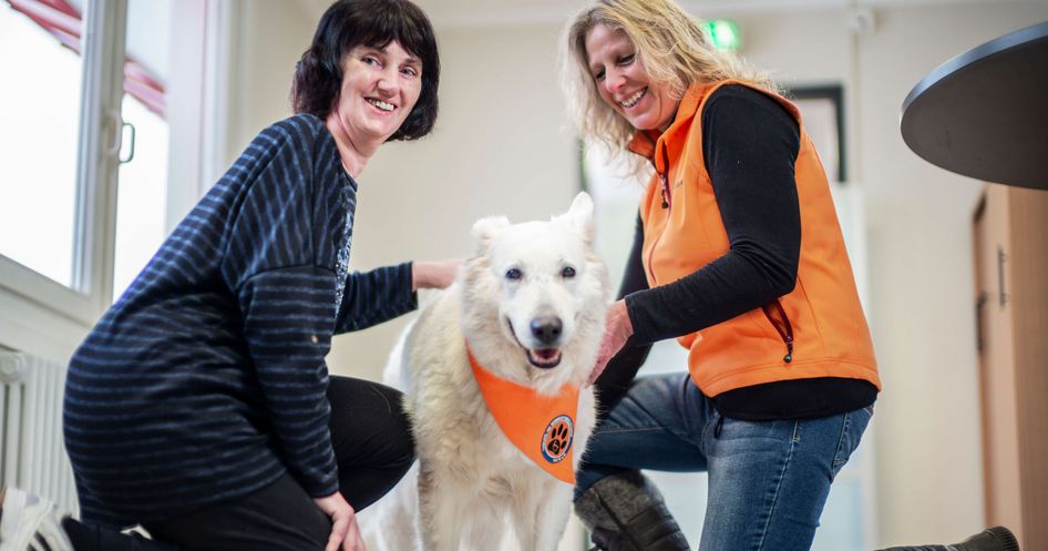 Patientin und Therapeutin herzen den weißen Therapiehund