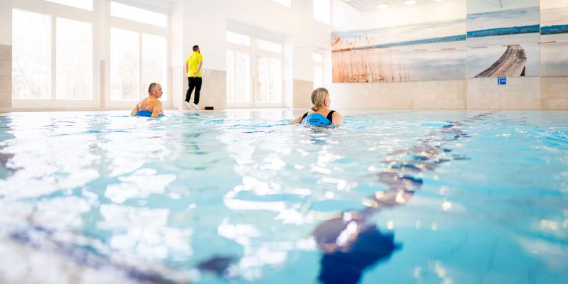 Ein Therapeut leitet zwei Patientinnen im Schwimmbad bei der Wassergymnastik an