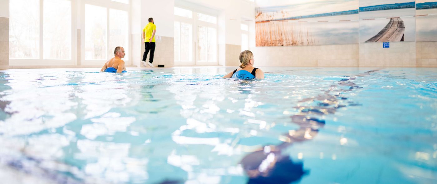 Ein Therapeut leitet zwei Patientinnen im Schwimmbad bei der Wassergymnastik an