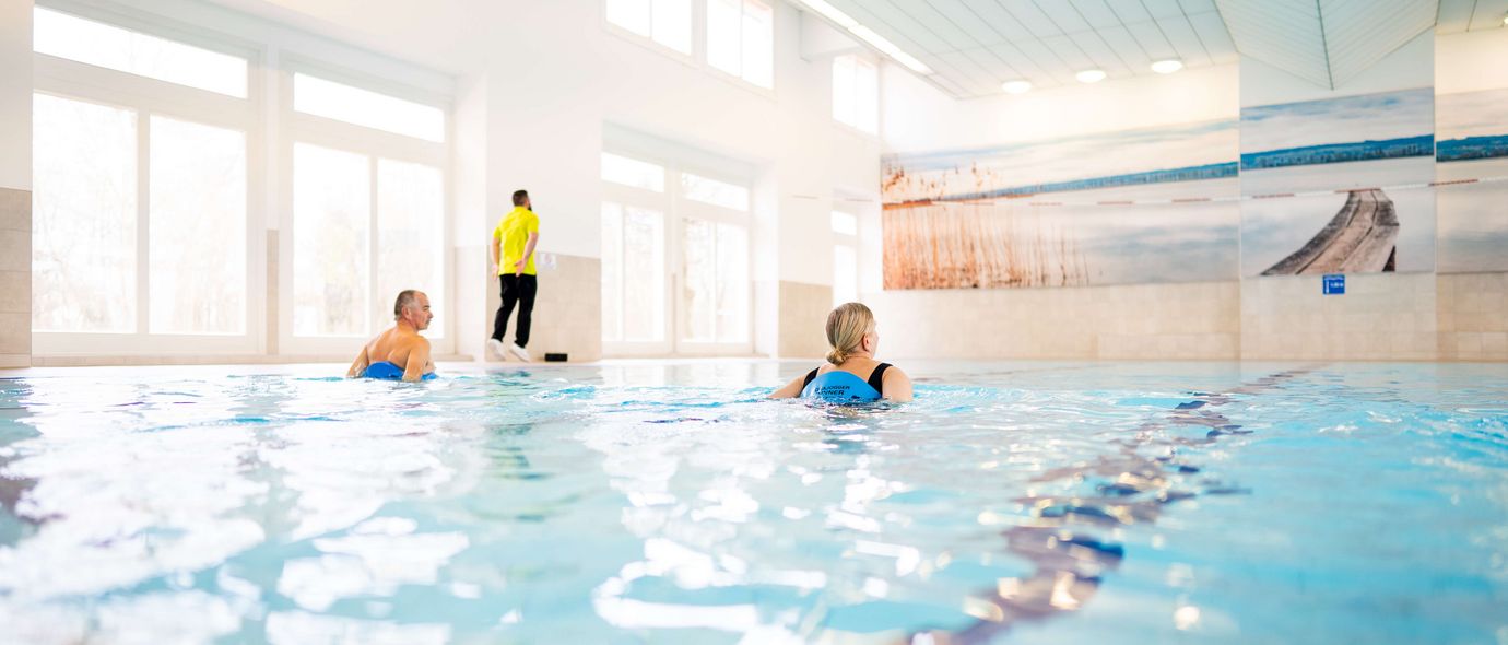 Ein Therapeut leitet zwei Patientinnen im Schwimmbad bei der Wassergymnastik an