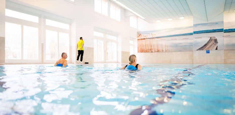 Ein Therapeut leitet zwei Patientinnen im Schwimmbad bei der Wassergymnastik an