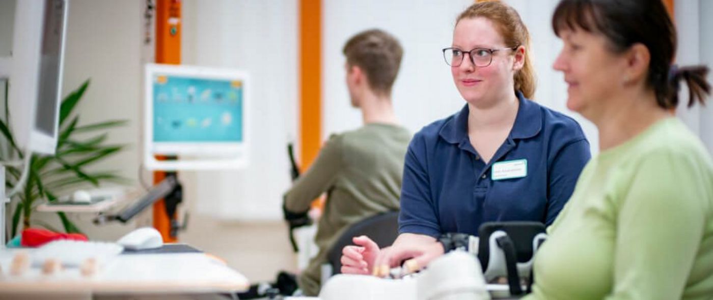 Eine Therapeutin zeigt einer Patientin mit einer Armverletzung Übungen am Gerät